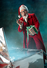 Image showing Modern stylish Santa Claus in red fashionable suit and cowboy\'s hat on dark background