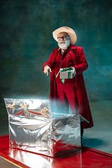 Image showing Modern stylish Santa Claus in red fashionable suit and cowboy\'s hat on dark background