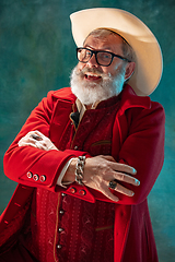 Image showing Modern stylish Santa Claus in red fashionable suit and cowboy\'s hat on dark background