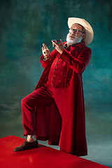 Image showing Modern stylish Santa Claus in red fashionable suit and cowboy\'s hat on dark background