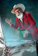 Image showing Modern stylish Santa Claus in red fashionable suit and cowboy\'s hat on dark background