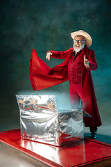 Image showing Modern stylish Santa Claus in red fashionable suit and cowboy\'s hat on dark background