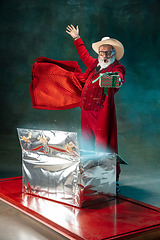 Image showing Modern stylish Santa Claus in red fashionable suit and cowboy\'s hat on dark background