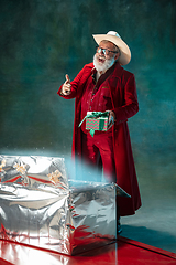 Image showing Modern stylish Santa Claus in red fashionable suit and cowboy\'s hat on dark background