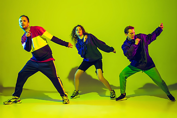 Image showing Stylish men and woman dancing hip-hop in bright clothes on gradient background at dance hall in neon light