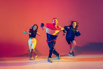 Image showing Stylish man and women dancing hip-hop in bright clothes on gradient background at dance hall in neon light