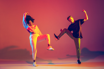 Image showing Stylish man and woman dancing hip-hop in bright clothes on gradient background at dance hall in neon light