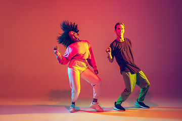 Image showing Stylish man and woman dancing hip-hop in bright clothes on gradient background at dance hall in neon light