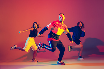 Image showing Stylish man and women dancing hip-hop in bright clothes on gradient background at dance hall in neon light