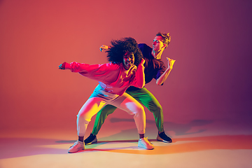 Image showing Stylish man and woman dancing hip-hop in bright clothes on gradient background at dance hall in neon light