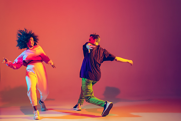 Image showing Stylish man and woman dancing hip-hop in bright clothes on gradient background at dance hall in neon light