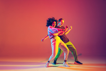 Image showing Stylish man and woman dancing hip-hop in bright clothes on gradient background at dance hall in neon light