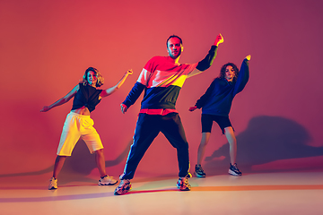 Image showing Stylish man and women dancing hip-hop in bright clothes on gradient background at dance hall in neon light