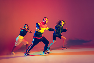 Image showing Stylish man and women dancing hip-hop in bright clothes on gradient background at dance hall in neon light