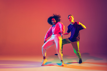 Image showing Stylish man and woman dancing hip-hop in bright clothes on gradient background at dance hall in neon light
