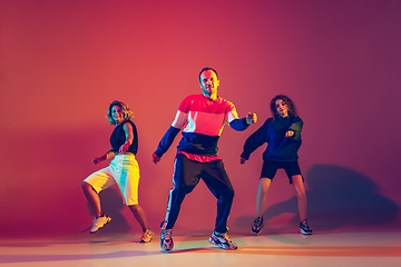 Image showing Stylish man and women dancing hip-hop in bright clothes on gradient background at dance hall in neon light