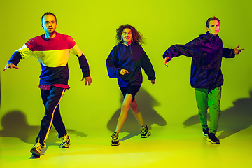 Image showing Stylish men and woman dancing hip-hop in bright clothes on gradient background at dance hall in neon light