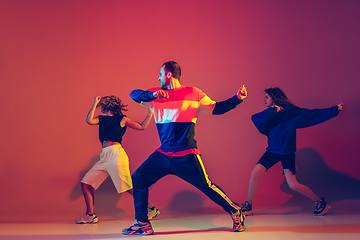 Image showing Stylish man and women dancing hip-hop in bright clothes on gradient background at dance hall in neon light