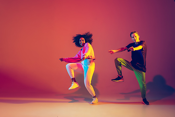 Image showing Stylish man and woman dancing hip-hop in bright clothes on gradient background at dance hall in neon light