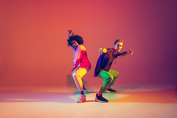 Image showing Stylish man and woman dancing hip-hop in bright clothes on gradient background at dance hall in neon light