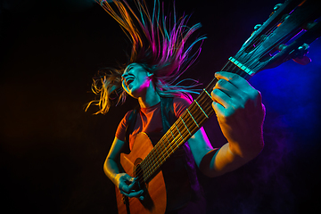 Image showing Playing guitar. Young woman with smoke and neon light on black background. Highly tensioned, wide angle, fish eye view