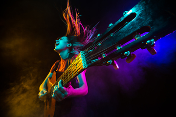 Image showing Playing guitar. Young woman with smoke and neon light on black background. Highly tensioned, wide angle, fish eye view