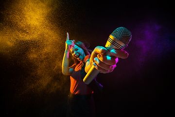 Image showing Singing with microphone. Young woman with smoke and neon light on black background. Highly tensioned, wide angle, fish eye view