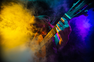 Image showing Playing guitar. Young woman with smoke and neon light on black background. Highly tensioned, wide angle, fish eye view