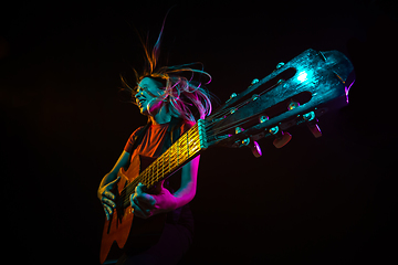 Image showing Playing guitar. Young woman with smoke and neon light on black background. Highly tensioned, wide angle, fish eye view