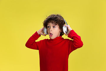 Image showing Pretty young curly boy in red wear on yellow studio background. Childhood, expression, fun.