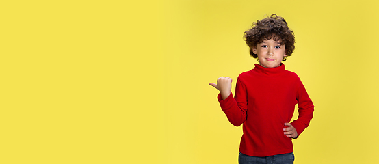 Image showing Pretty young curly boy in red wear on yellow studio background. Childhood, expression, fun.