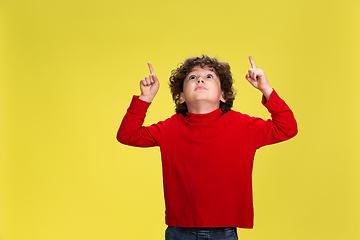 Image showing Pretty young curly boy in red wear on yellow studio background. Childhood, expression, fun.