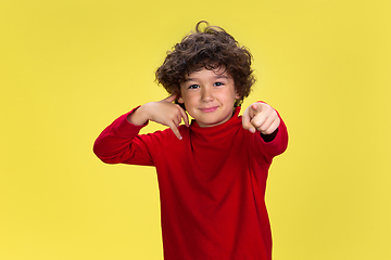 Image showing Pretty young curly boy in red wear on yellow studio background. Childhood, expression, fun.