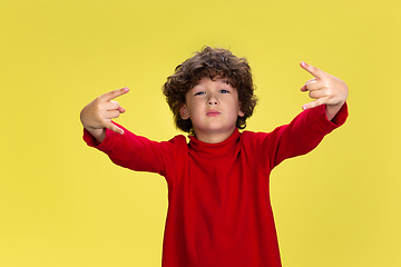 Image showing Pretty young curly boy in red wear on yellow studio background. Childhood, expression, fun.