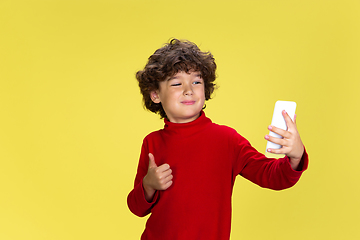 Image showing Pretty young curly boy in red wear on yellow studio background. Childhood, expression, fun.