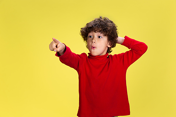 Image showing Pretty young curly boy in red wear on yellow studio background. Childhood, expression, fun.