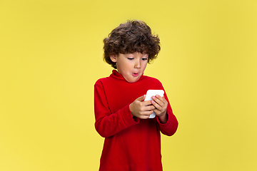 Image showing Pretty young curly boy in red wear on yellow studio background. Childhood, expression, fun.