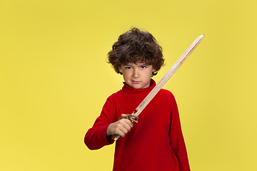 Image showing Pretty young curly boy in red wear on yellow studio background. Childhood, expression, fun.