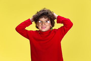 Image showing Pretty young curly boy in red wear on yellow studio background. Childhood, expression, fun.
