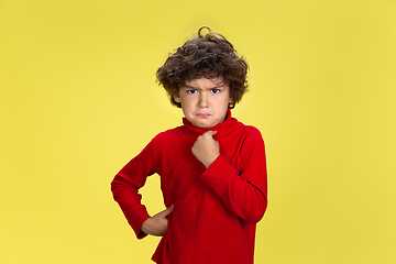 Image showing Pretty young curly boy in red wear on yellow studio background. Childhood, expression, fun.