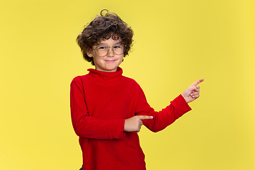 Image showing Pretty young curly boy in red wear on yellow studio background. Childhood, expression, fun.