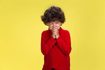 Image showing Pretty young curly boy in red wear on yellow studio background. Childhood, expression, fun.