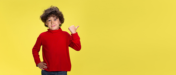 Image showing Pretty young curly boy in red wear on yellow studio background. Childhood, expression, fun.