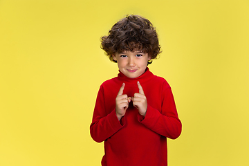 Image showing Pretty young curly boy in red wear on yellow studio background. Childhood, expression, fun.