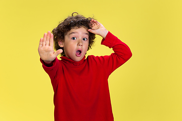 Image showing Pretty young curly boy in red wear on yellow studio background. Childhood, expression, fun.