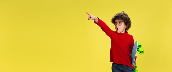 Image showing Pretty young curly boy in red wear on yellow studio background. Childhood, expression, fun.