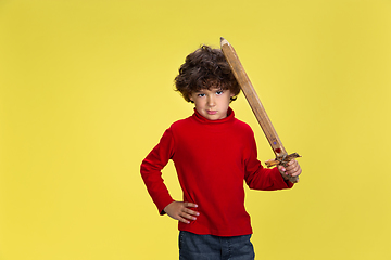 Image showing Pretty young curly boy in red wear on yellow studio background. Childhood, expression, fun.