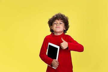 Image showing Pretty young curly boy in red wear on yellow studio background. Childhood, expression, fun.