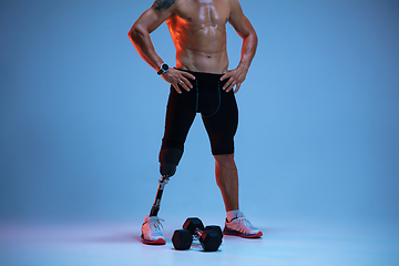 Image showing Athlete with disabilities or amputee isolated on blue studio background. Professional male sportsman with leg prosthesis training with weights in neon