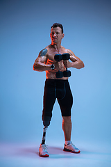 Image showing Athlete with disabilities or amputee isolated on blue studio background. Professional male sportsman with leg prosthesis training with weights in neon